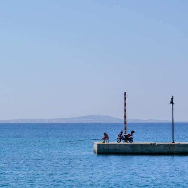 Photo d'un pêcheur solitaire au bout d'une jetée sur une ile grecque